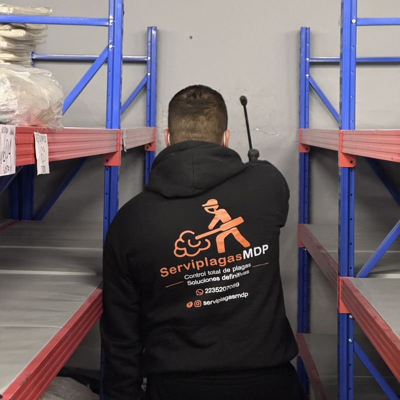 Técnico de ServiplagasMDP aplicando producto entre estanterías de un depósito
